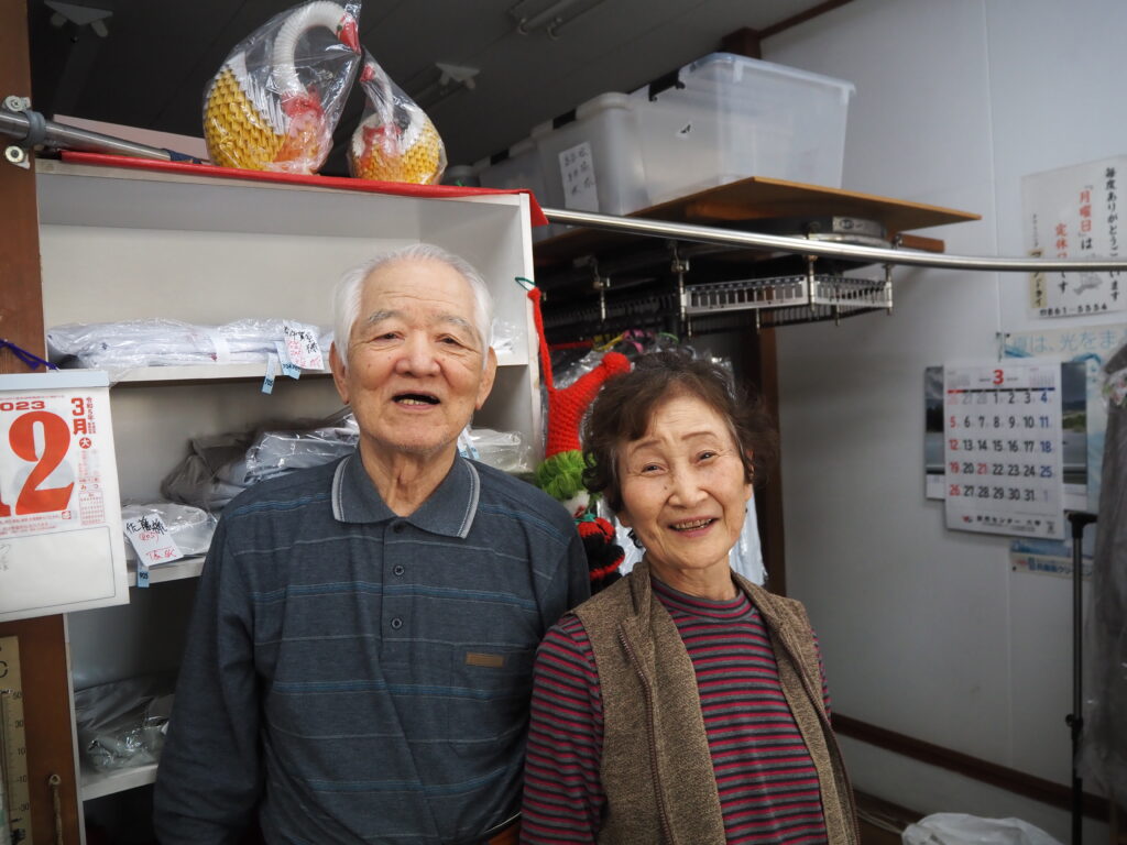 田中勝利さん・田中冴子さんがお店の中で笑って寄り添っている写真