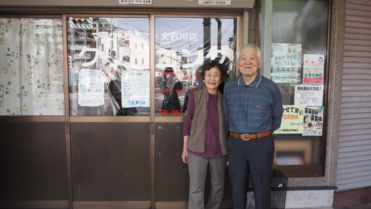 田中勝利さん・田中冴子さんがお店の前で笑って寄り添っている写真